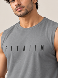 A close-up of a man wearing a gray sleeveless muscle tank top with the word 'FITAIIM' printed in black across the chest, set against a plain beige background.