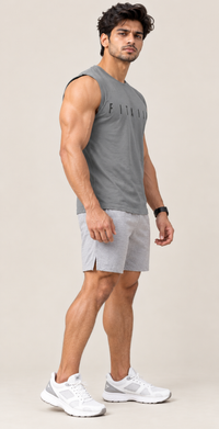A man modeling a gray sleeveless athletic tank top and light gray shorts with white sneakers, standing against a plain beige studio background.