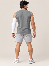 A man shown from the back wearing a gray sleeveless athletic tank top, light gray shorts, white sneakers, and a white compression sleeve on one arm, against a plain beige studio background.