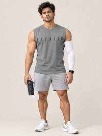 A muscular man modeling a gray sleeveless athletic t-shirt with 'FITAIIM' printed across the chest, paired with gray shorts, white sneakers, and a white arm sleeve, holding a black shaker bottle against a solid beige background.