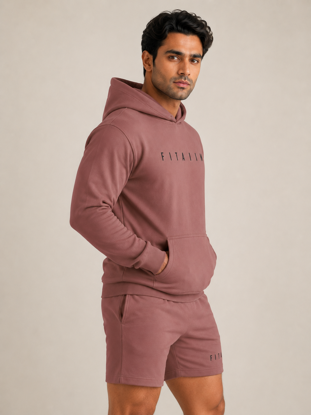 A man modeling a coral matching loungewear set consisting of a pullover hoodie and shorts, featuring the brand name 'FITAIIM' printed on the chest and leg.