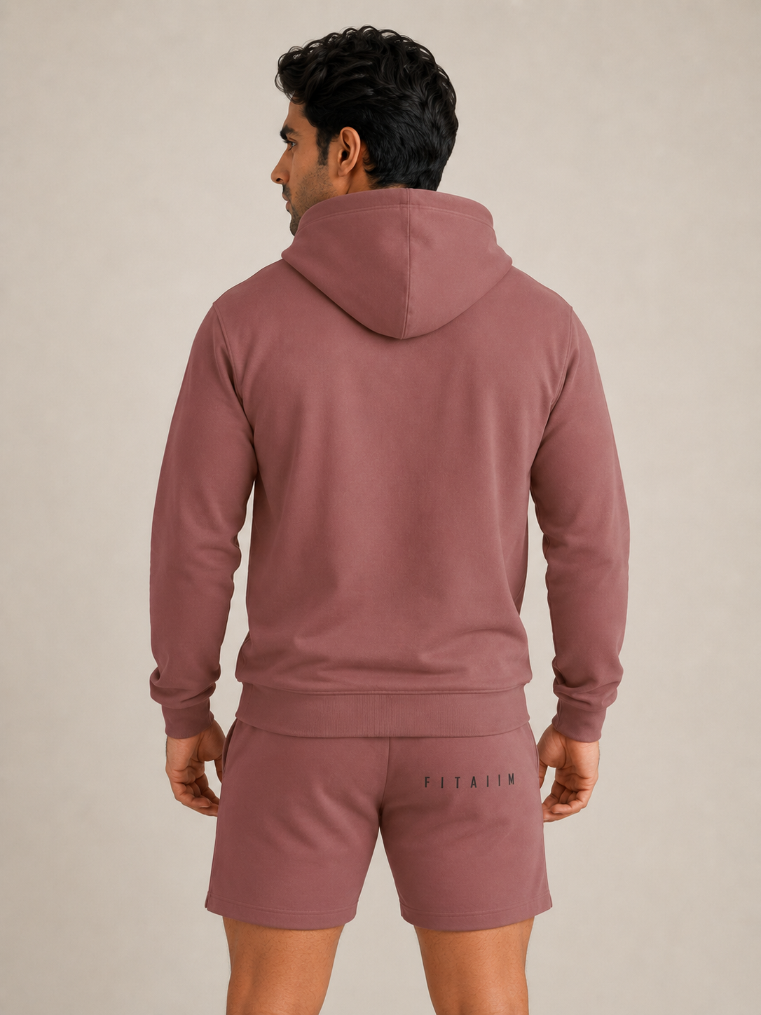 A man shown from the back wearing a dcoral  hoodie and matching sweat shorts against a neutral beige studio background. The shorts feature the brand name 'FITAIIM' printed on the back.