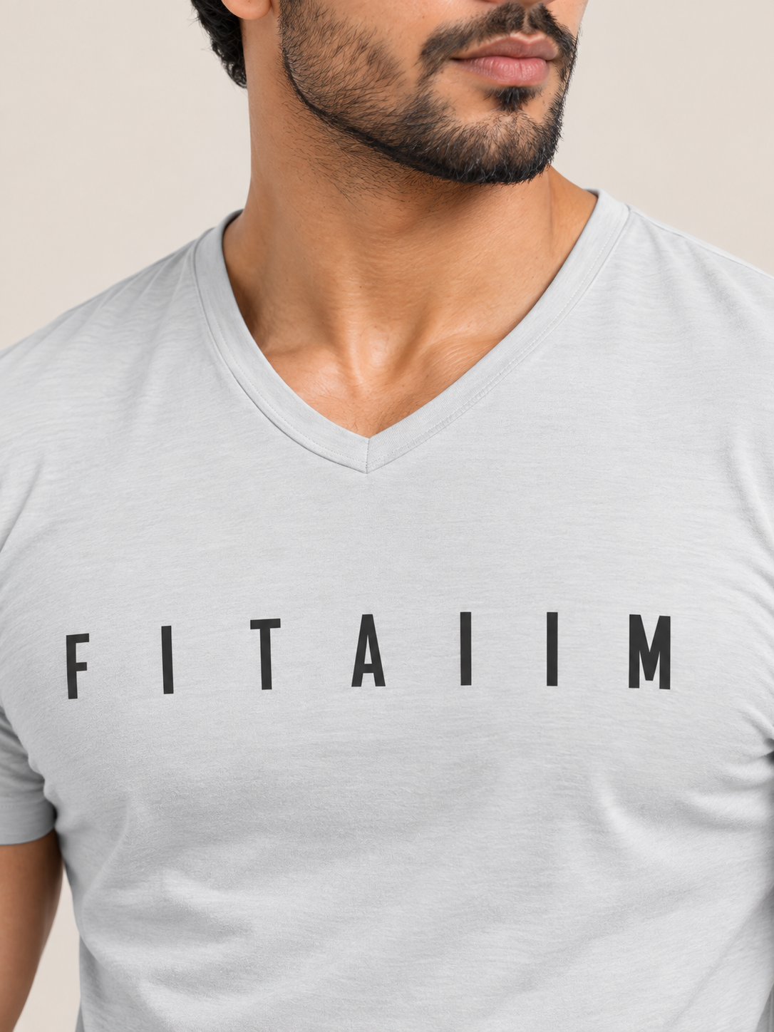 A close-up of a man wearing a light gray heathered v-neck t-shirt with the word 'FITAIIM' printed in black capital letters across the chest.
