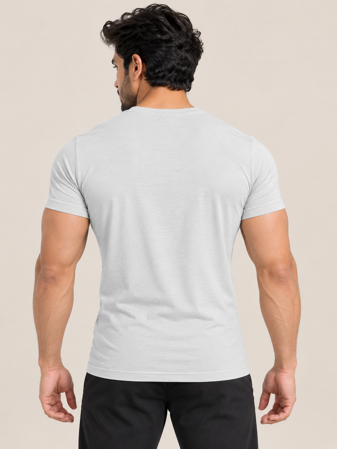A man viewed from behind wearing a light gray short-sleeve crewneck t-shirt and black pants, set against a solid beige background.