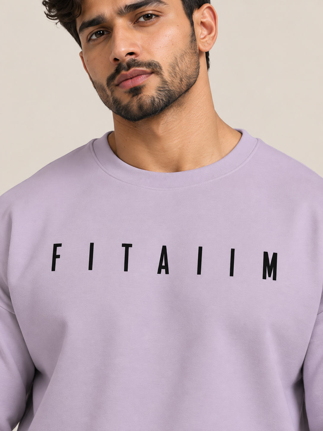 A close-up of a man wearing a lavender crewneck sweatshirt with the word 'FITAIIM' printed in black across the chest.