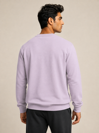 A man shown from the back wearing a light PINK crewneck sweatshirt and black pants, standing against a plain beige studio background.