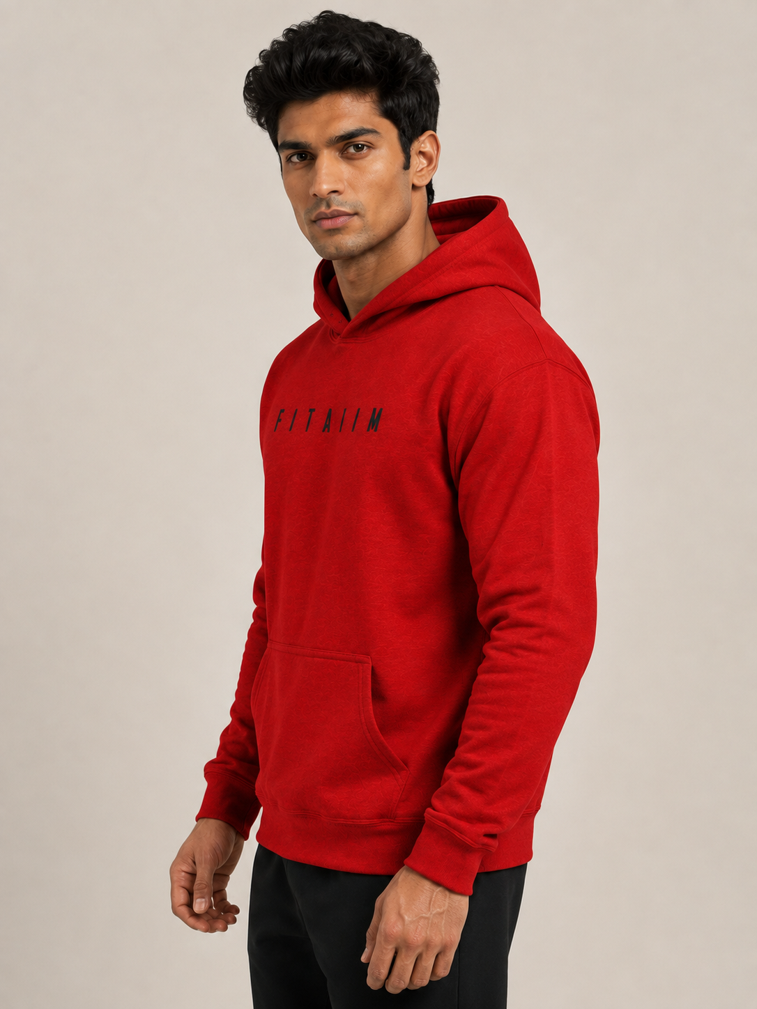 A man wearing a bright red pullover hoodie with the word 'FITAIIM' printed in black across the chest, posed against a solid light gray studio background.