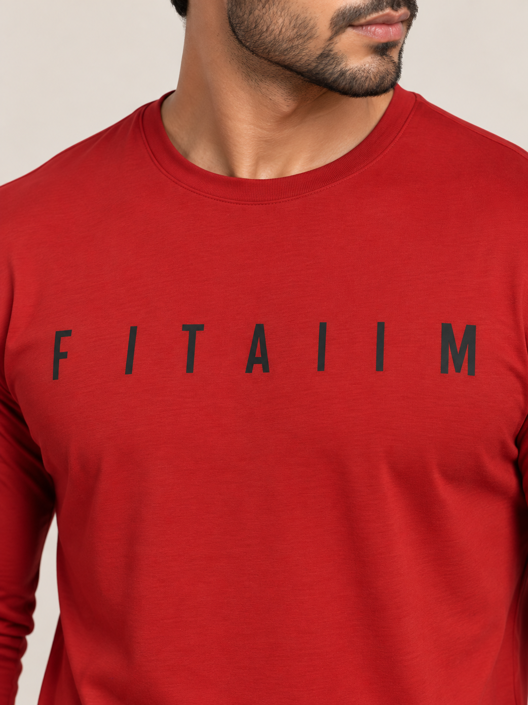 A close-up of a man wearing a red long-sleeve t-shirt with the name 'FITAIIM' printed in black across the chest, set against a plain light beige background.