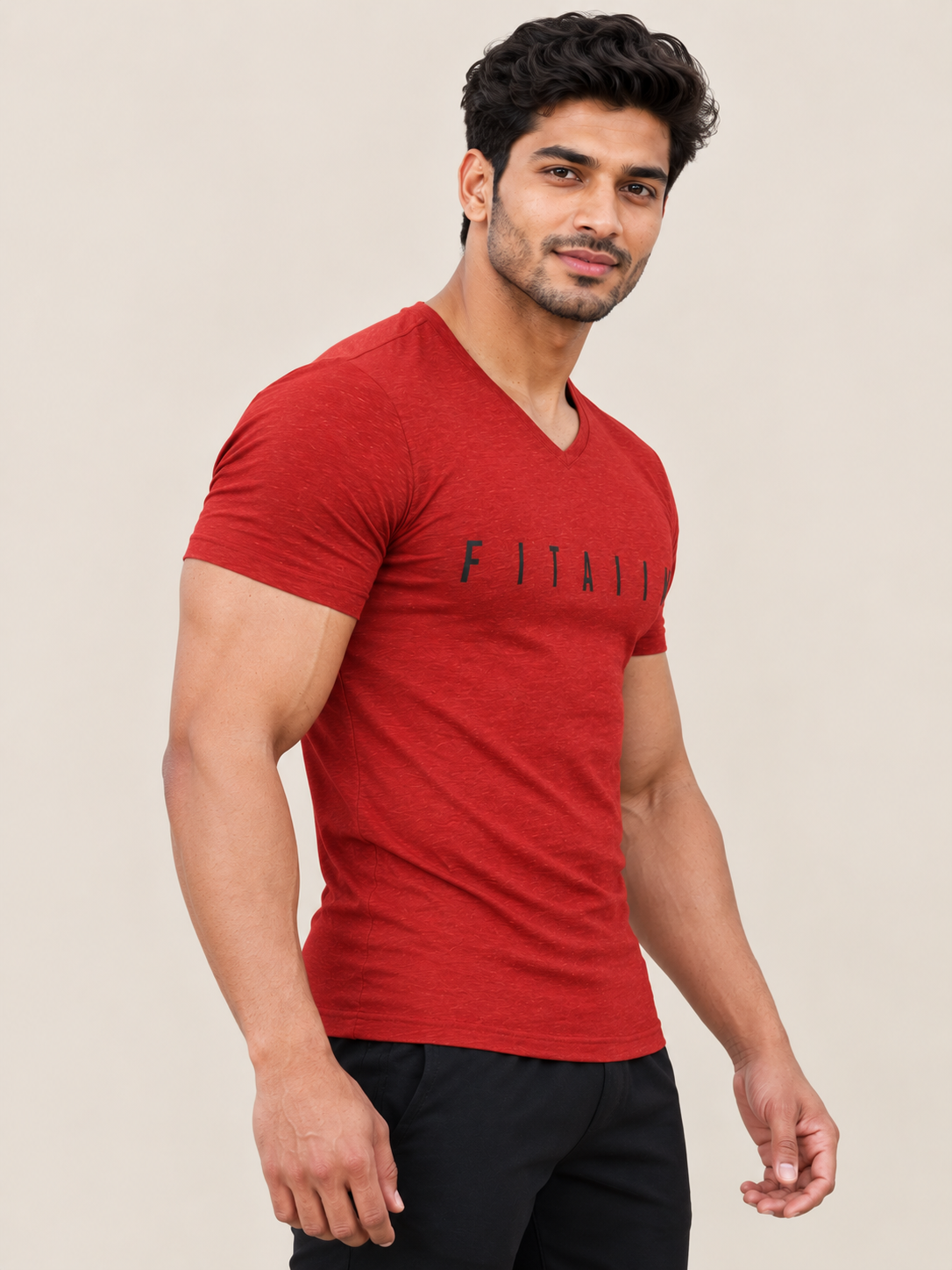 A muscular man wearing a RED v-neck t-shirt with the brand name 'FITAIIM' printed in black across the chest, paired with black pants, set against a solid beige background.