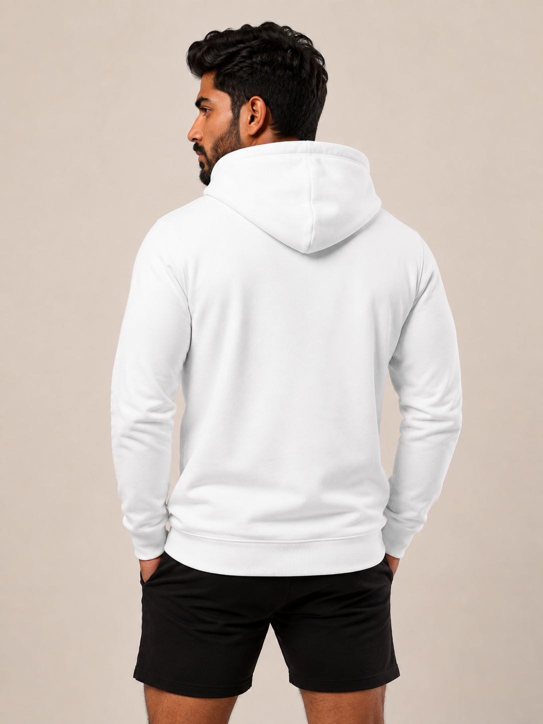 A man shown from the back wearing a plain white pullover hoodie and black athletic shorts, standing against a solid light beige studio background.
