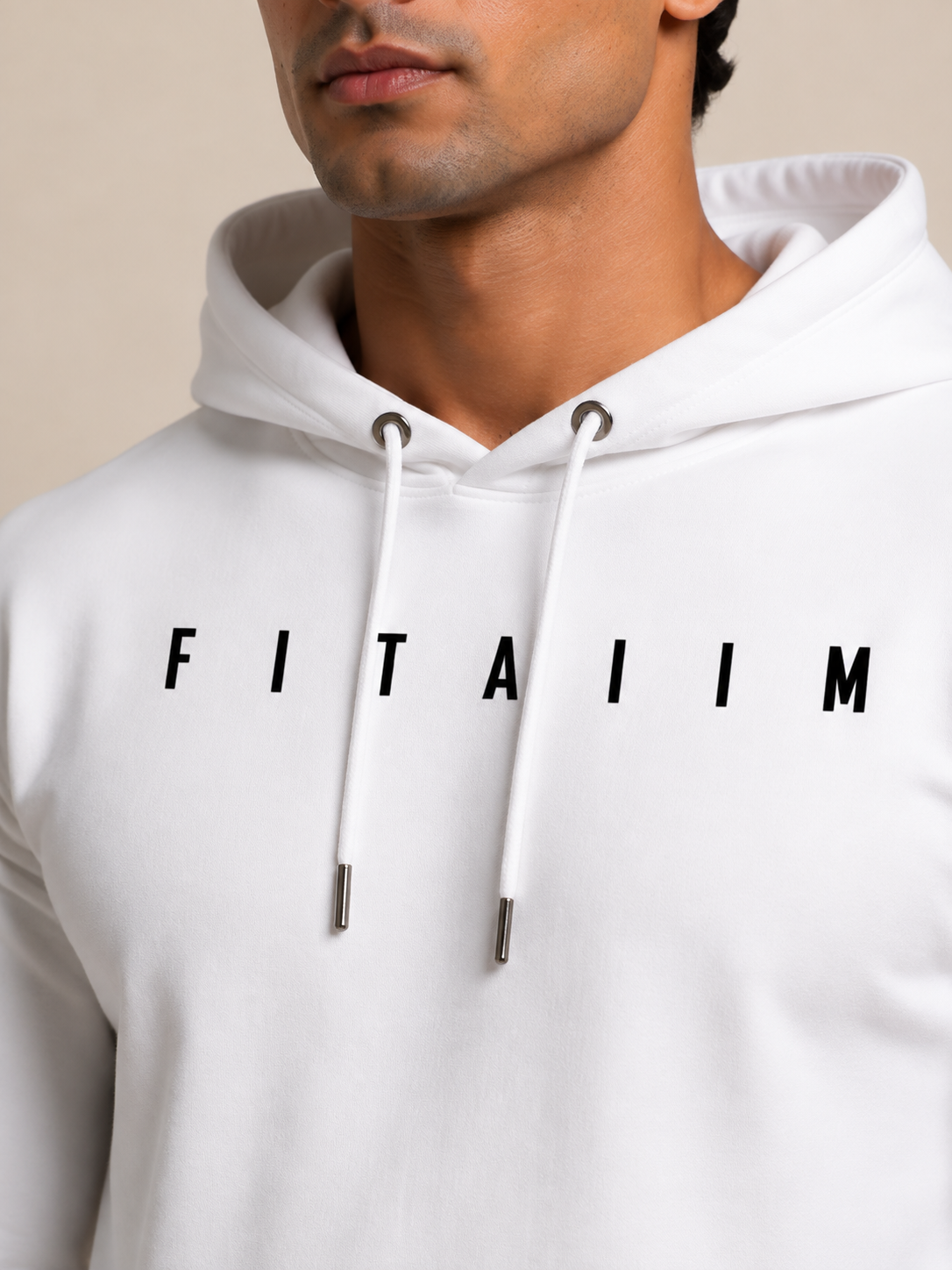 A close-up of a man wearing a white pullover hoodie with the word 'FITAIIM' printed in black across the chest. The hoodie has white drawstrings with silver metal tips and is photographed against a plain beige background.