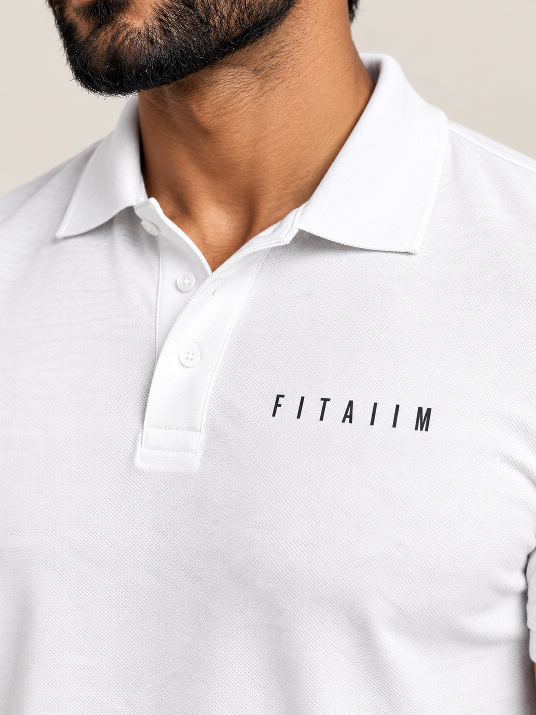 A close-up of a man wearing a white short-sleeve polo shirt with the brand name 'FITAIIM' printed in black on the left chest.
