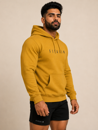 A man wearing a mustard yellow FITAIIM pullover hoodie and black FITAIIM athletic shorts, standing against a plain beige studio background.