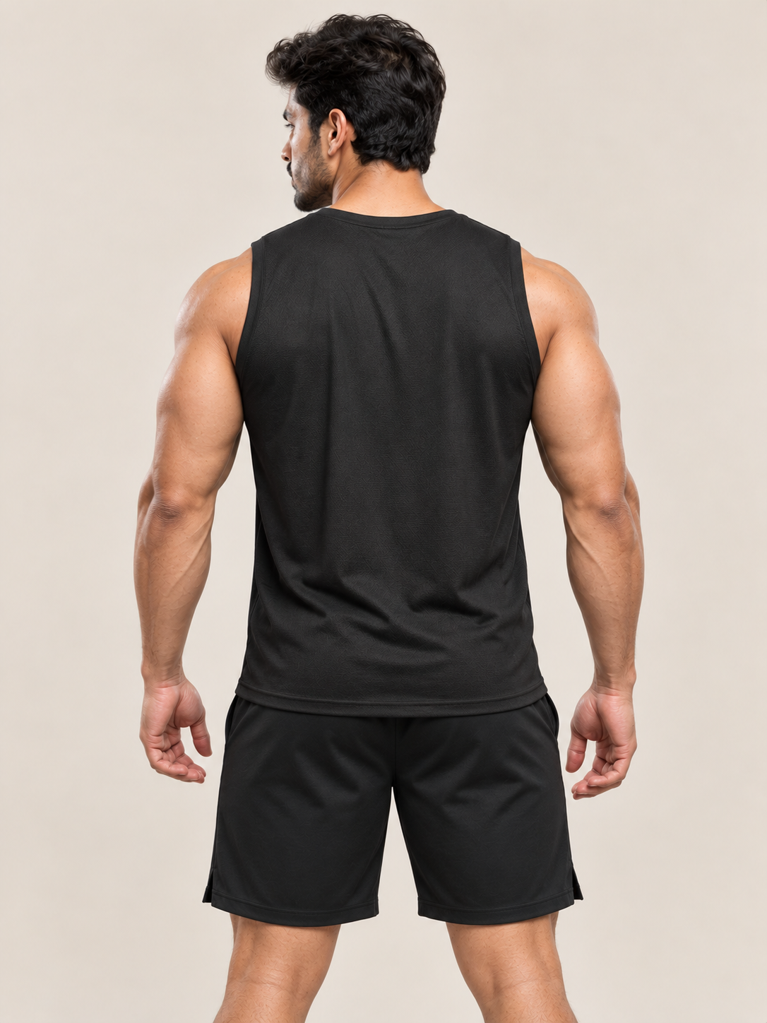 A muscular man shown from the back wearing a black sleeveless athletic tank top and matching black shorts against a plain beige studio background.