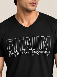 A man wearing a black V-neck t-shirt with 'FITAIIM Better Than Yesterday' printed in white across the chest, shown in a close-up shot against a light beige background.