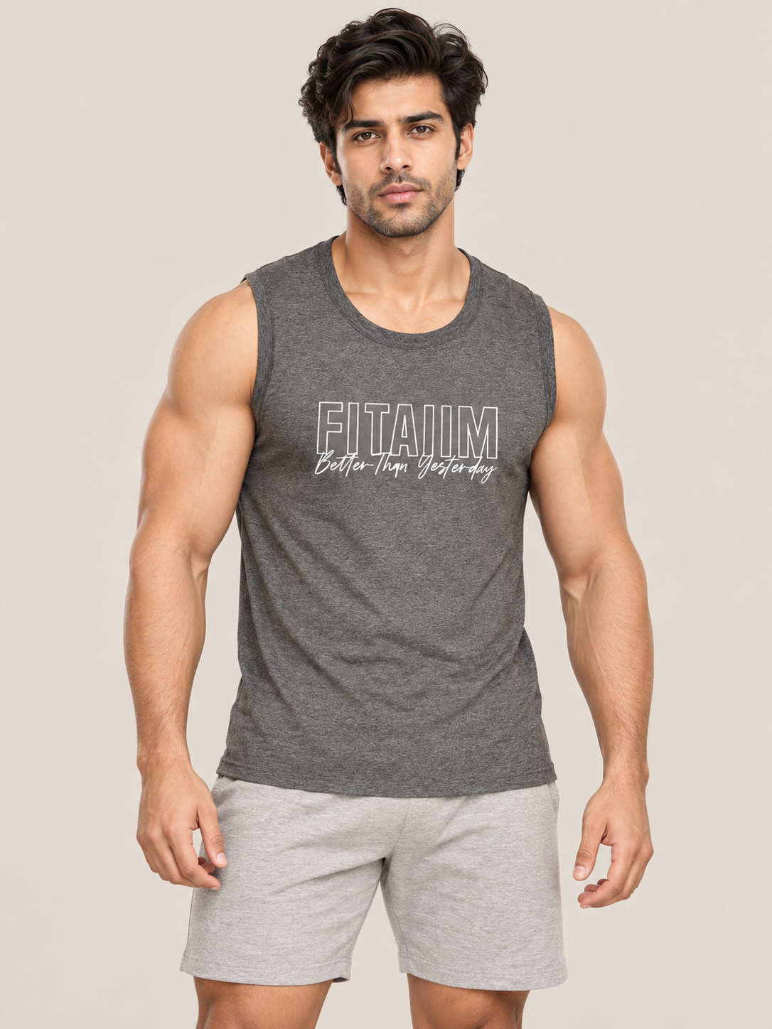 A muscular man wearing a dark gray sleeveless tank top with 'FITAIIM Better-than-Yesterday' printed on the chest, paired with light gray shorts, against a solid beige background.