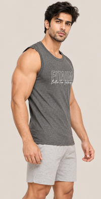 A muscular man wearing a dark gray sleeveless athletic tank top with 'FITAIIM Better Then Yesterday' printed on the front, paired with light gray shorts, against a solid beige background.