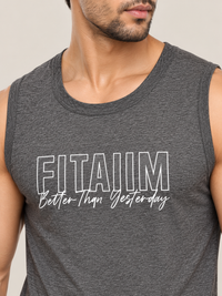 A close-up of a man wearing a dark heather gray sleeveless tank top with the text 'FITAIIM Better Than Yesterday' printed in white on the chest, set against a plain light beige background.