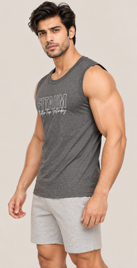A muscular man wearing a dark gray sleeveless tank top with 'FITAIM' printed on the chest and light gray shorts, posed against a solid light beige background.