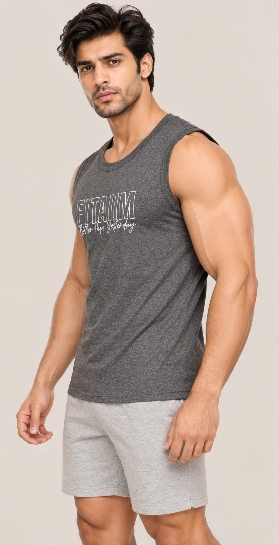 A muscular man wearing a dark gray sleeveless tank top with 'FITAIM' printed on the chest and light gray shorts, posed against a solid light beige background.