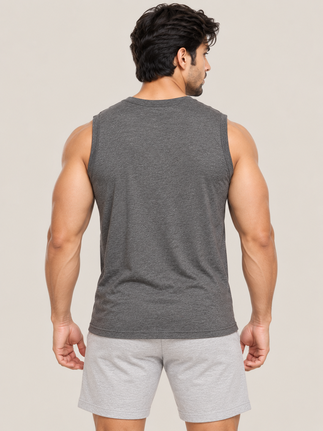 A man shown from the back wearing a dark gray sleeveless muscle tank top and light gray athletic shorts against a solid light beige background.