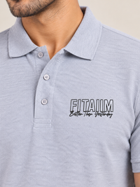 Close-up of a man wearing a grey polo shirt with a white embroidered logo on the left chest that reads 'FITAIIIM Better Than Yesterday'.