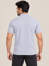 A man viewed from the back wearing a light gray short-sleeve polo shirt and black pants, standing against a plain beige studio background.