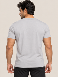 A muscular man viewed from the back wearing a plain grey short-sleeve crewneck t-shirt and black pants, set against a solid light beige background.