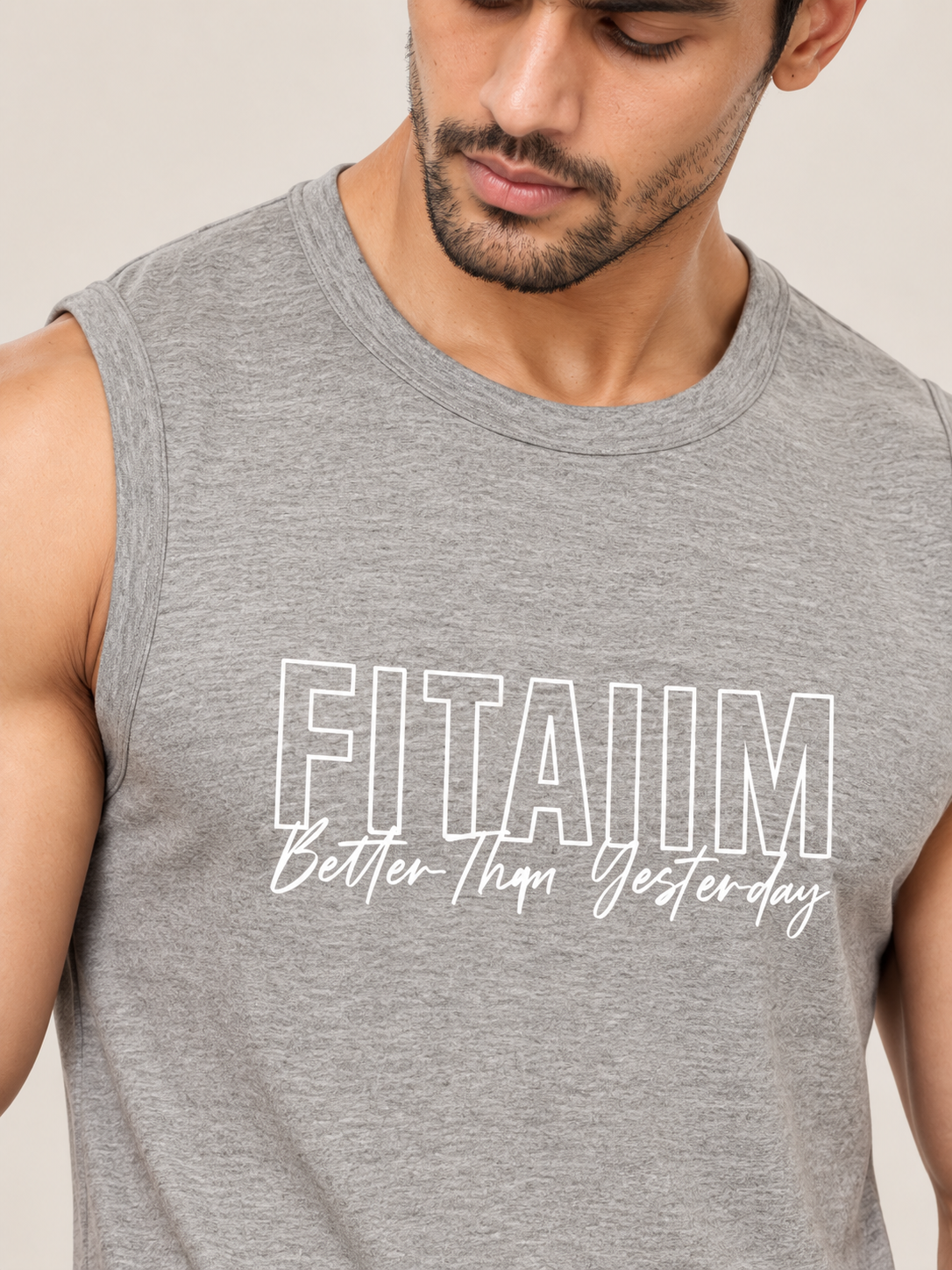 A close-up of a man wearing a heather gray sleeveless tank top with the text 'FITAIIM Better Than Yesterday' printed in white on the front, against a plain light beige background.