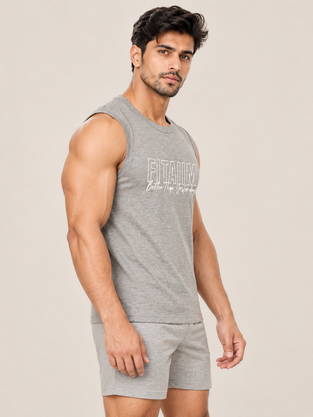A muscular man wearing a heather gray sleeveless tank top with 'FITAIIM Better Then Yesterday' printed in white on the chest, paired with matching gray shorts, set against a solid light beige background.