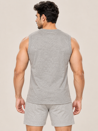 A muscular man viewed from the back wearing a heather gray sleeveless tank top and matching heather gray shorts against a plain beige studio background.