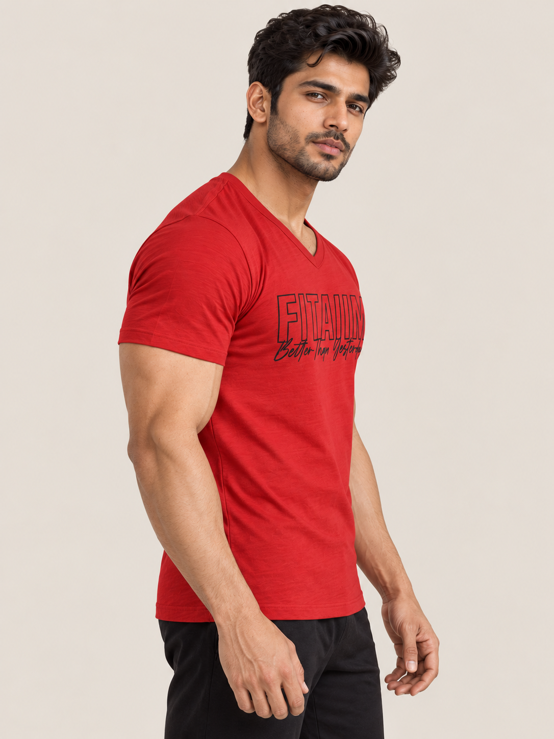 A muscular man wearing a RED v-neck t-shirt with a BLACK graphic print that reads 'FITAIIM BETTER THEN YESTERDAY' and black pants, standing against a solid light beige background.