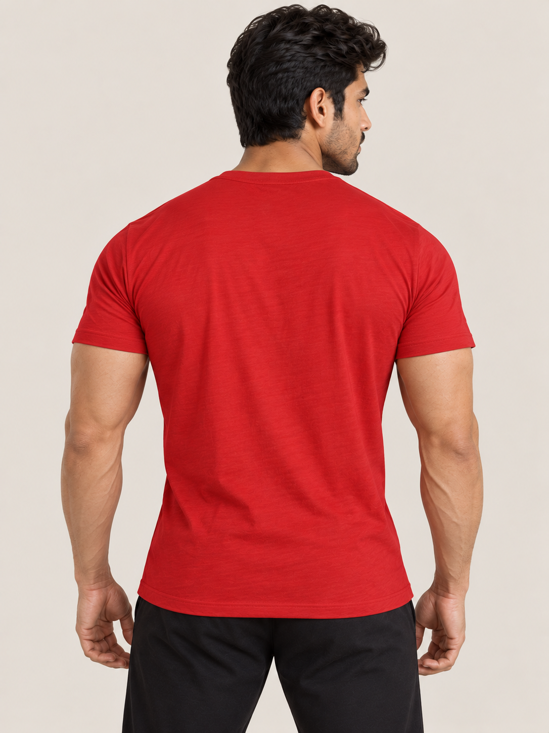 A muscular man viewed from the back wearing a plain RED short-sleeve crewneck t-shirt and black pants, set against a solid light beige background.