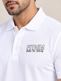 A close-up of a man wearing a white short-sleeve polo shirt with a black and white 'FITAIIM Better Than Yesterday' graphic printed on the left chest, set against a plain beige background.