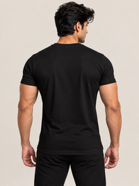 A man viewed from behind wearing a solid black short-sleeve crewneck t-shirt and white pants, set against a plain beige studio background.