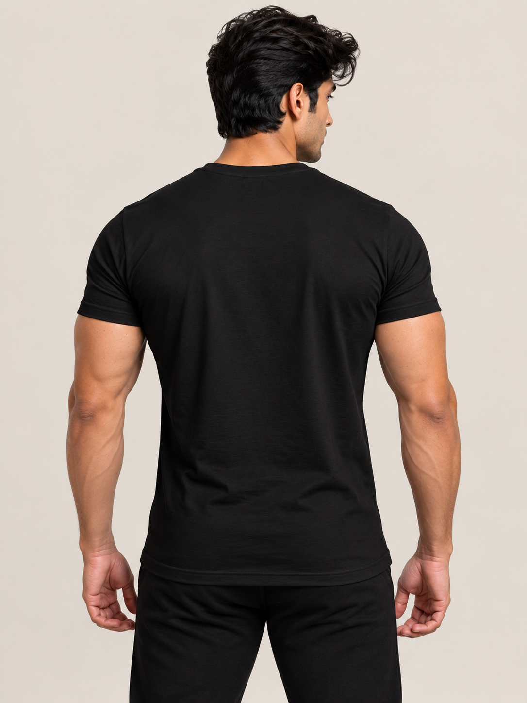 A man viewed from behind wearing a solid black short-sleeve crewneck t-shirt and white pants, set against a plain beige studio background.