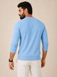 A man wearing a light blue long-sleeve crewneck sweatshirt, shown from the back against a solid beige studio background.