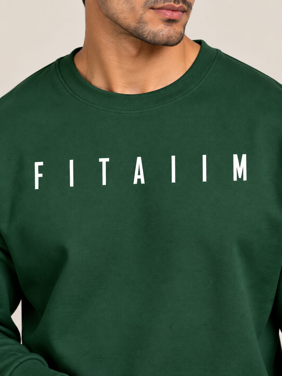 A close-up of a man wearing a green crewneck sweatshirt with the name 'FITAIIM' printed in bold white capital letters across the chest, set against a plain beige background.