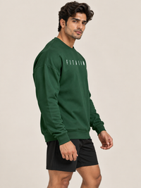 A man modelling a green two-piece tracksuit with white 'FITAIM' text on the sweatshirt and shorts, paired with white sneakers, against a solid beige studio background.