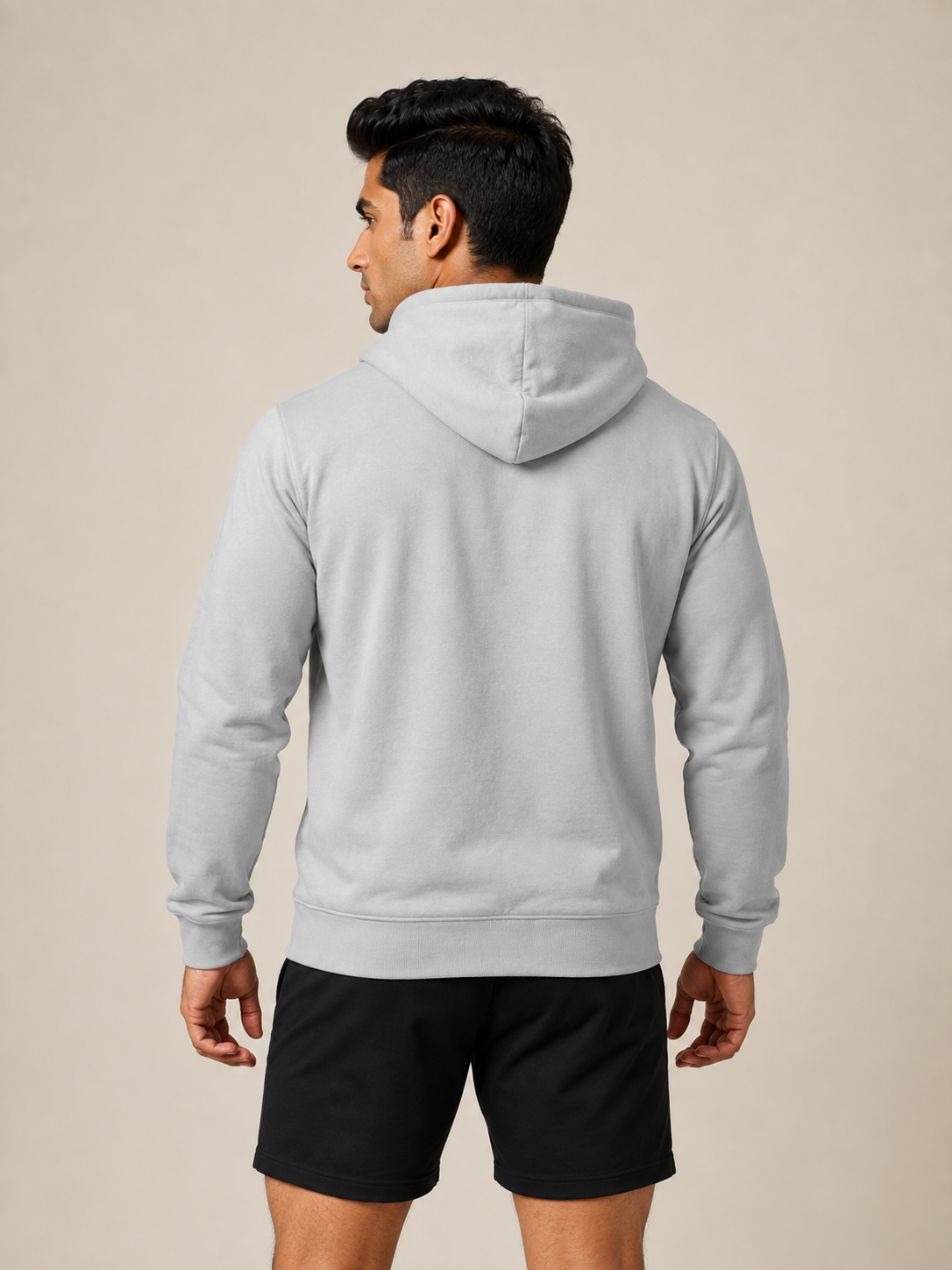 A man shown from the back wearing a light gray pullover hoodie and black athletic shorts, standing against a plain beige studio background.