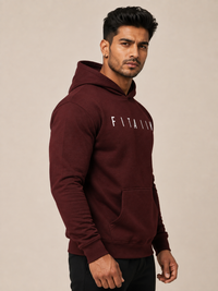 A man wearing a maroon pullover hoodie with 'FITAIIM' printed in white across the chest, posed against a solid beige background.