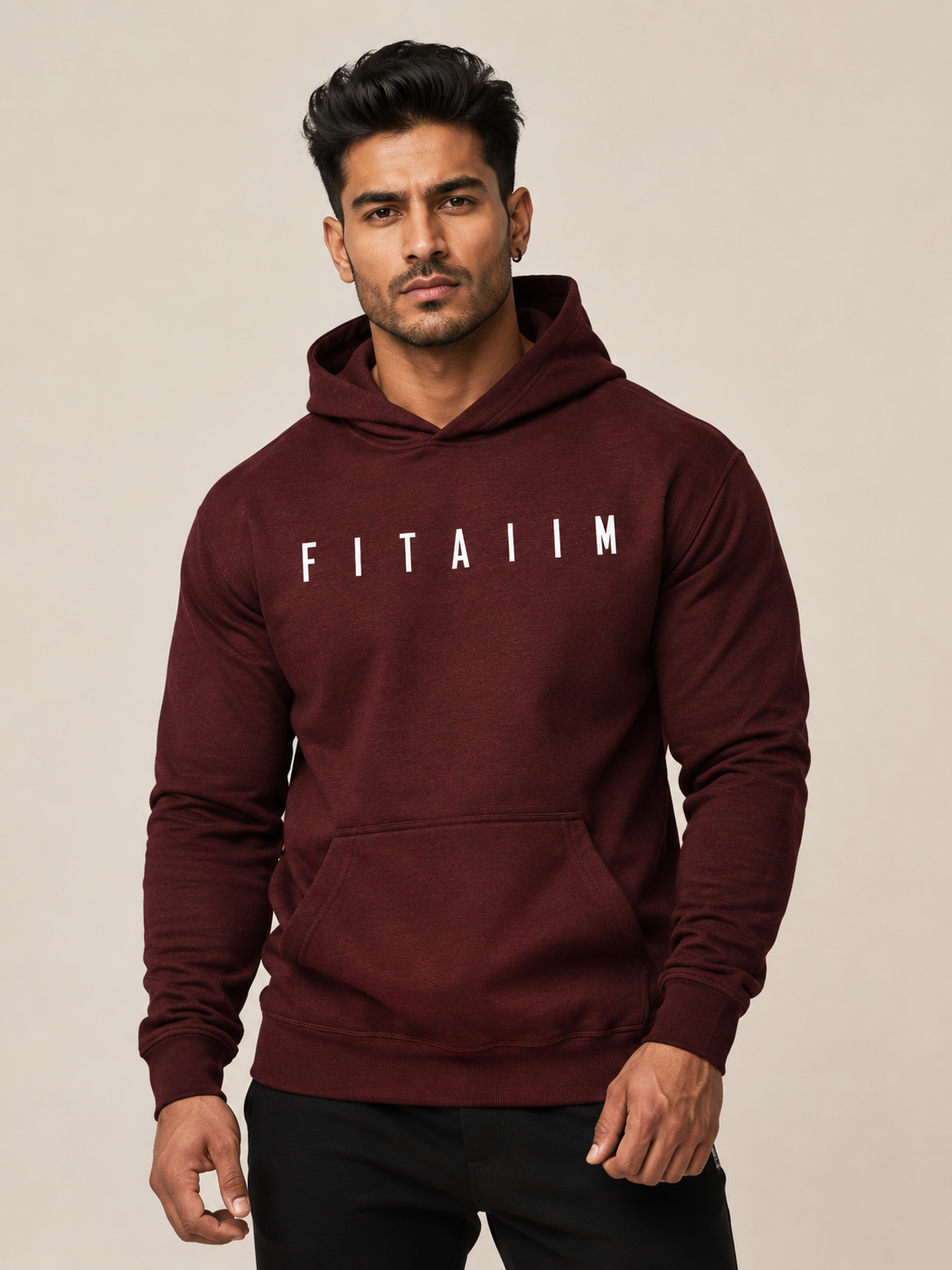 A man wearing a maroon pullover hoodie with 'FITAIIM' printed in white across the chest, paired with black pants, against a plain beige studio background.