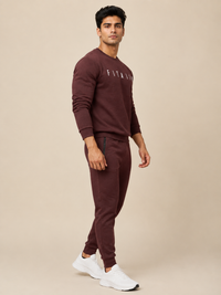 A man wearing a maroon sweatshirt with a white 'FITAIIM' graphic on the chest, paired with beige pants, photographed against a neutral beige studio background.