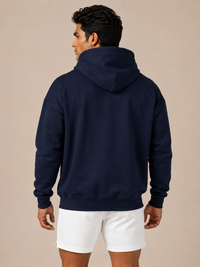 A man shown from the back wearing a navy blue pullover hoodie and white shorts, standing against a solid beige studio background.