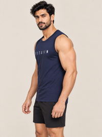 A muscular man wearing a navy blue sleeveless athletic tank top with 'FITAIIM' printed in white across the chest, paired with black athletic shorts, photographed against a solid light beige background.