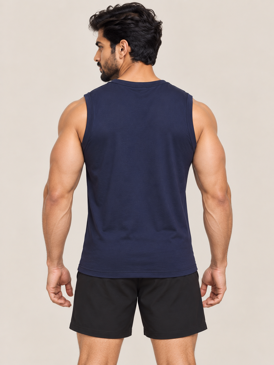 A muscular man shown from the back wearing a navy blue sleeveless athletic tank top and black shorts, set against a plain beige studio background.