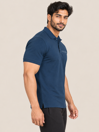 A man wearing a navy blue short-sleeve polo shirt with a small white embroidered logo on the left chest, paired with black trousers, set against a solid light beige background.
