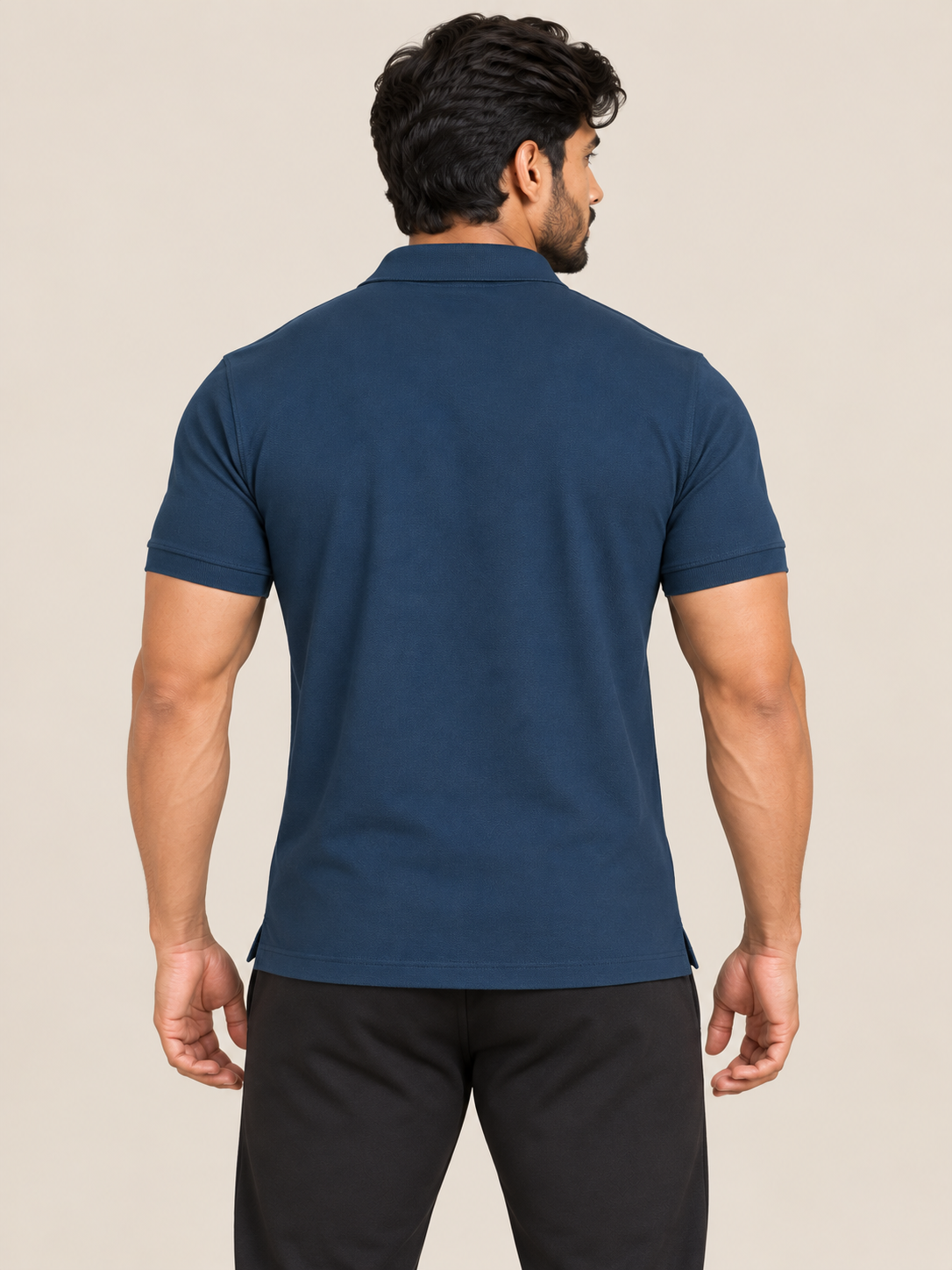 A man shown from the back wearing a navy blue short-sleeve polo shirt and black pants, standing against a plain light beige studio background.
