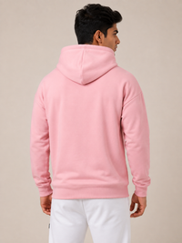 A man wearing a light pink pullover hoodie, shown from the back and side against a plain beige studio background.