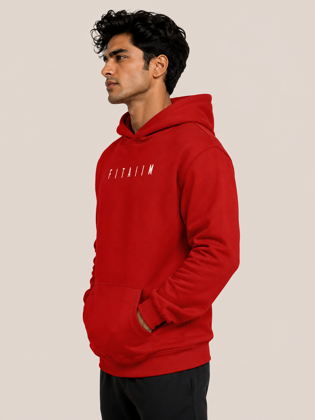 A man wearing a bright red pullover hoodie with 'FITBILIM' printed in white across the chest, shown in a side-profile view against a solid light beige background.
